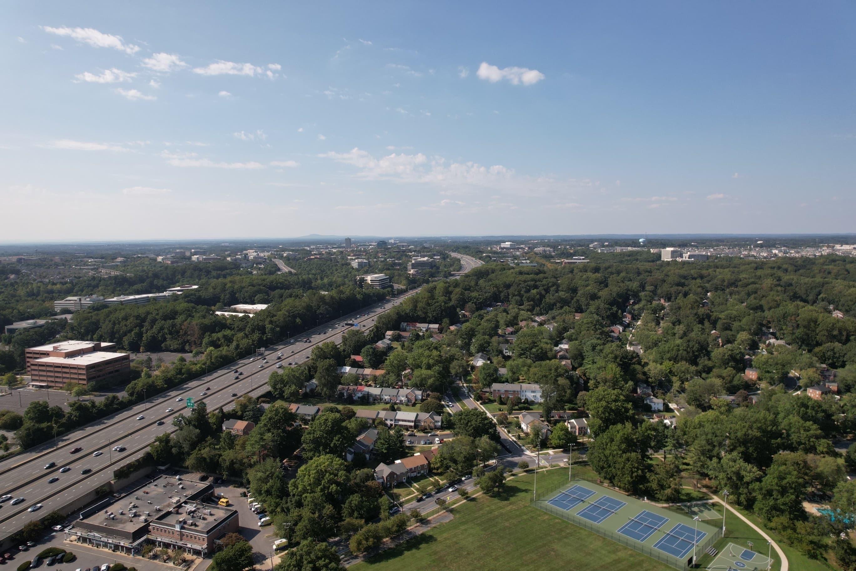 Overhead view of Gaithersburg, MD featuring homes on tree-lined streets, a large green field, and a busy interstate.