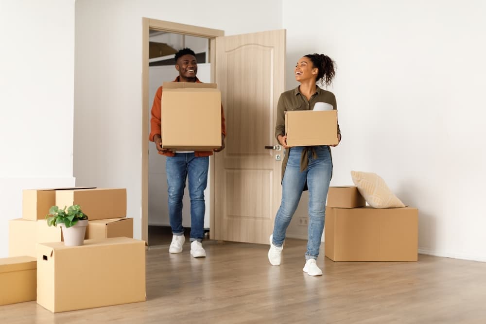 2 people carrying moving boxes into a new home