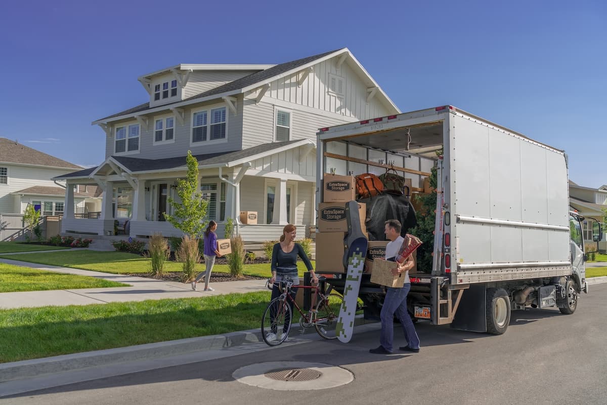 A family unloading a moving truck with a house in the background