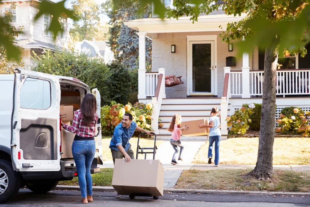 A family unloading moving boxes from a moving van into their new home