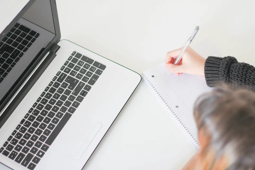 Woman writing on a notebook next to a laptop