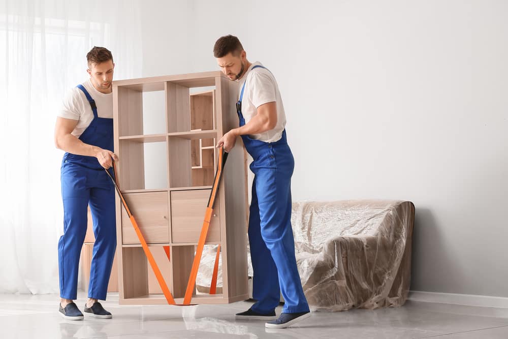 Two movers inside using lifting straps to move living room bookshelf