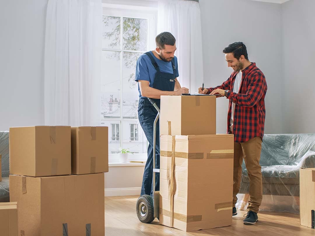 2 men with moving boxes on a dolly inside of a home