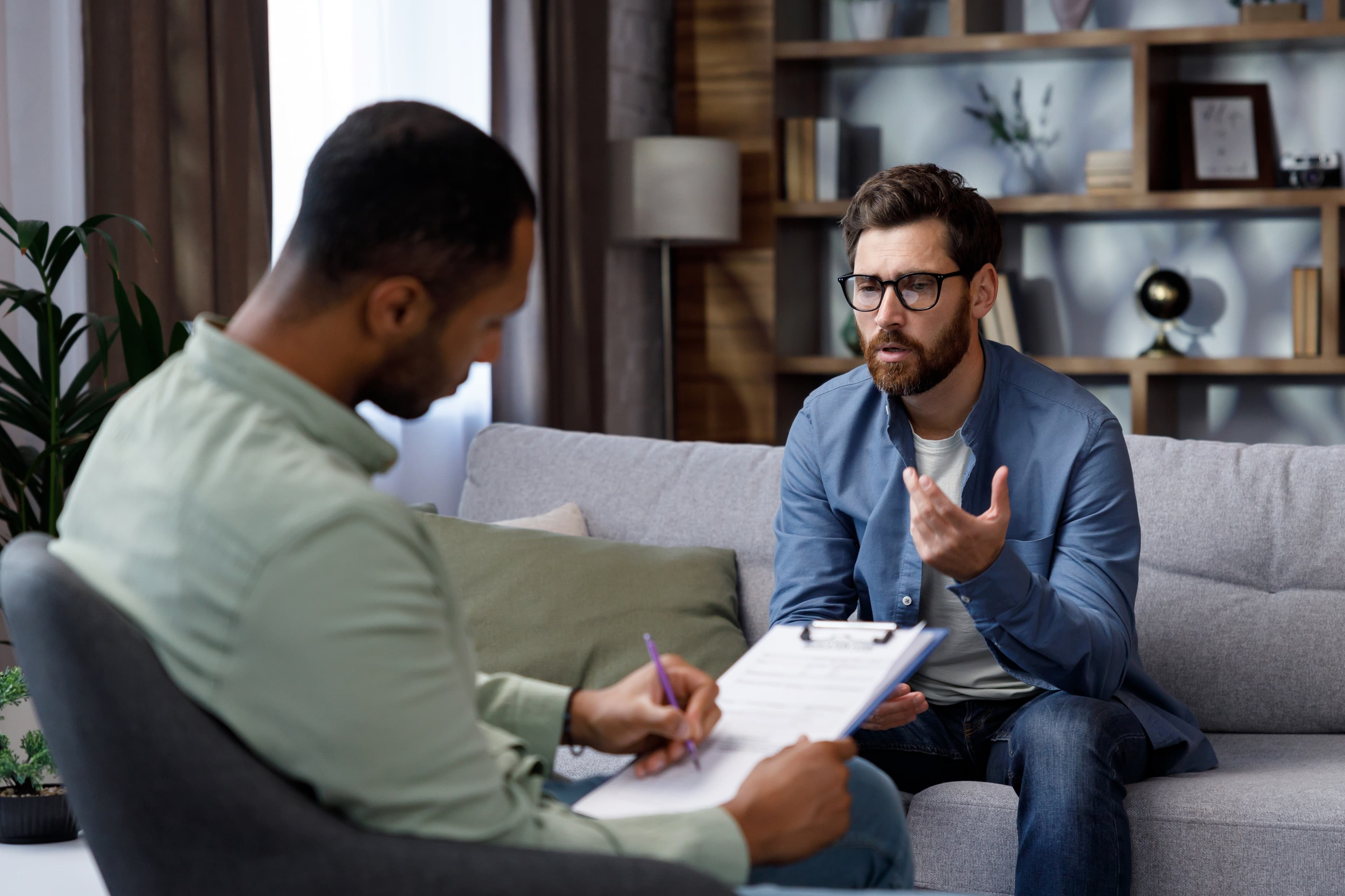 Therapist taking notes on a clipboard while a client speaks during a counseling session
