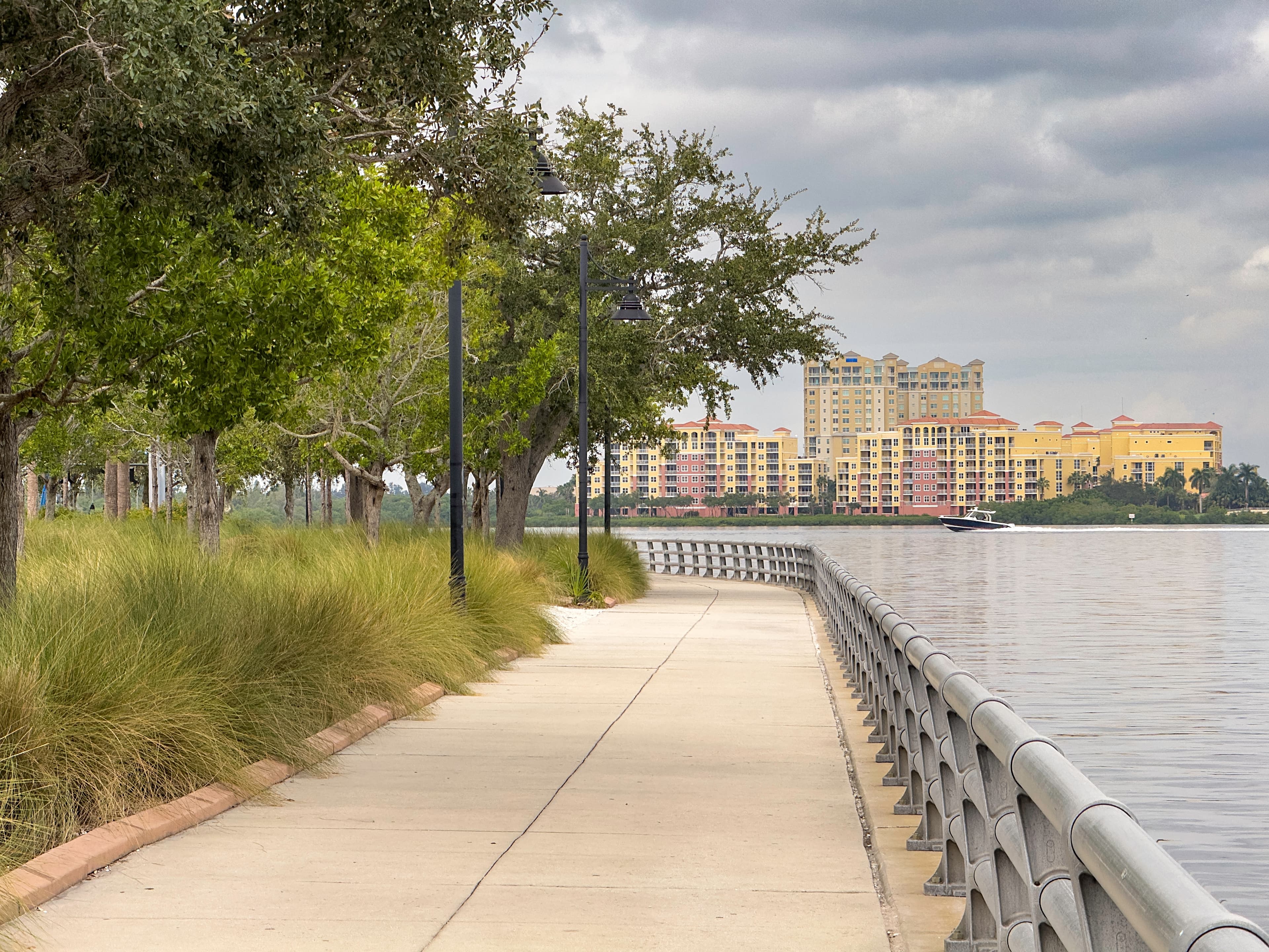 A greenery-lined path along the water during daytime in Bradenton, FL, with buildings in the background.