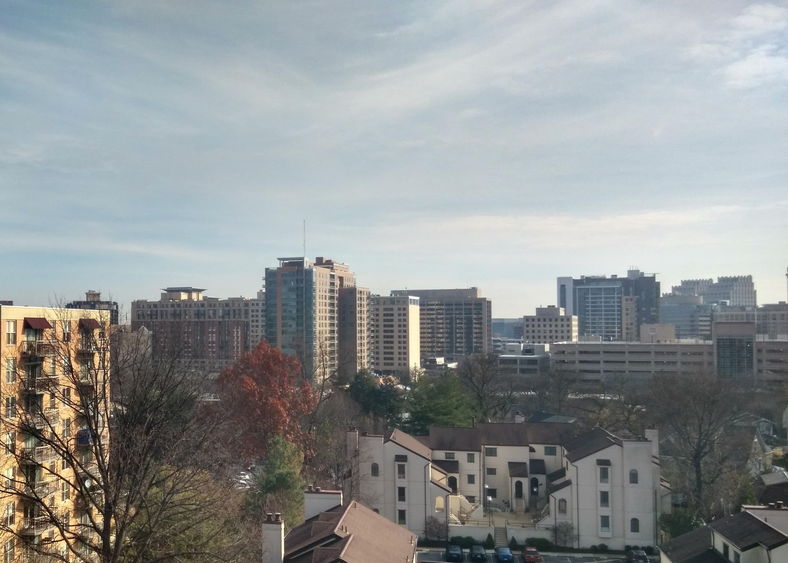 Skyline photo of Bethesda, MD featuring many buildings, trees, and a partly cloudy sky.