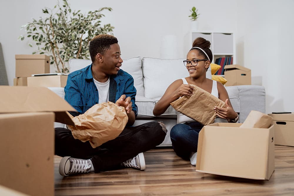 A couple sitting on the floor packing things into moving boxes