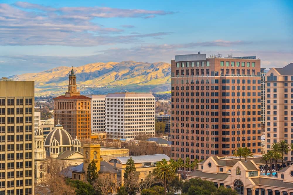 Aerial image of San Jose, CA's cityscape, with blue skies and mountains in the background.