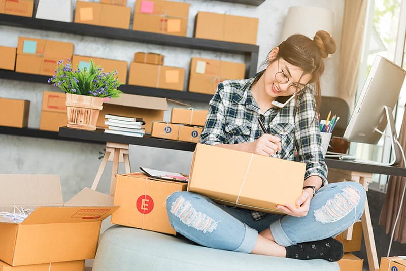 Woman sitting on the phone and writing label on box
