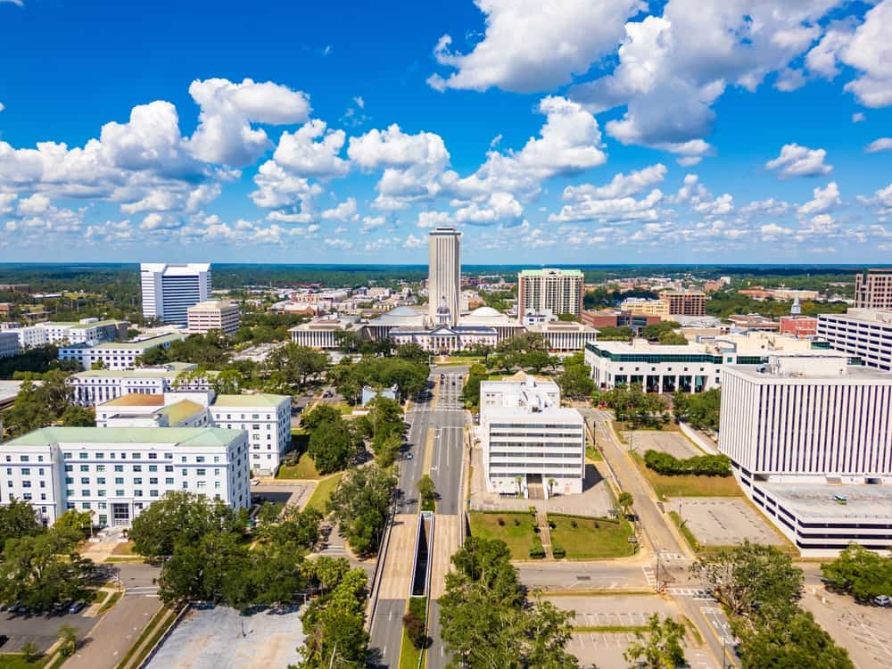 Aerial view of Tallahassee’s downtown area featuring the Florida State Capitol complex, surrounding government buildings, and tree-lined streets.