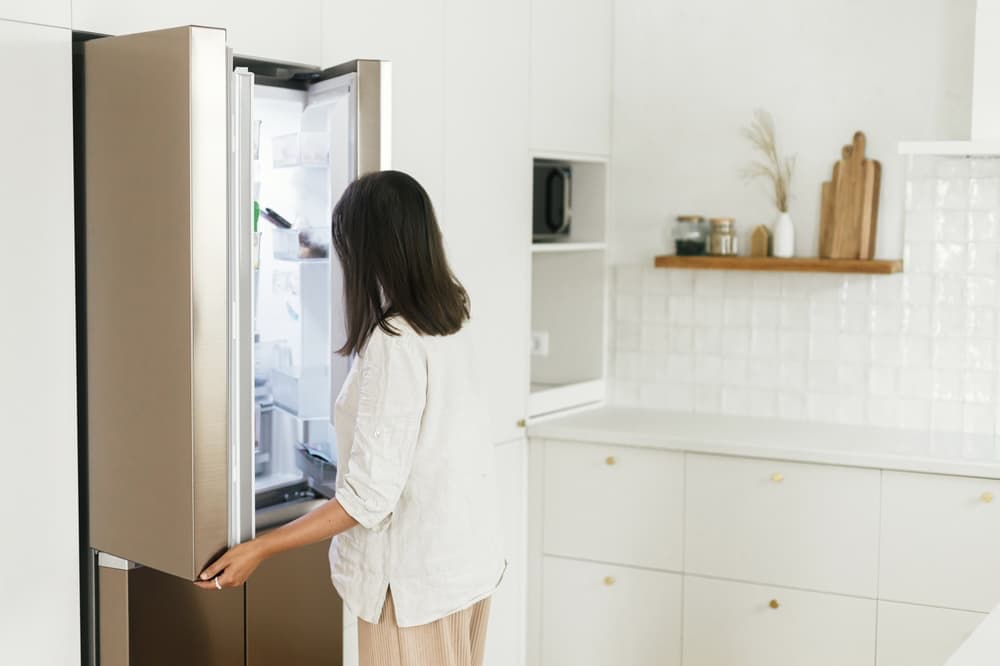 A woman opening a refrigerator in a bright, clean kitchen.