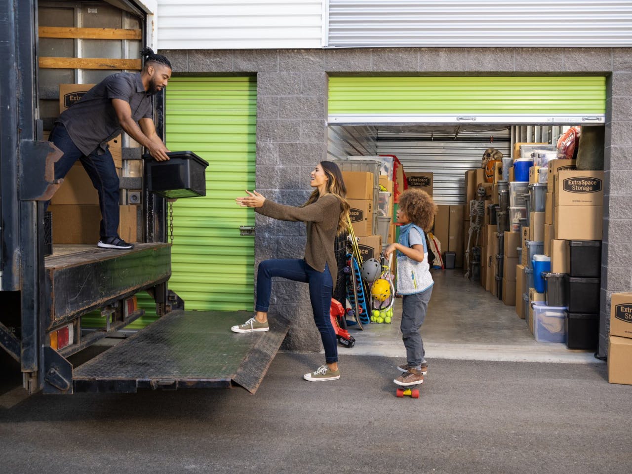 Family of three unloading boxes out of a moving truck into a storage unit 