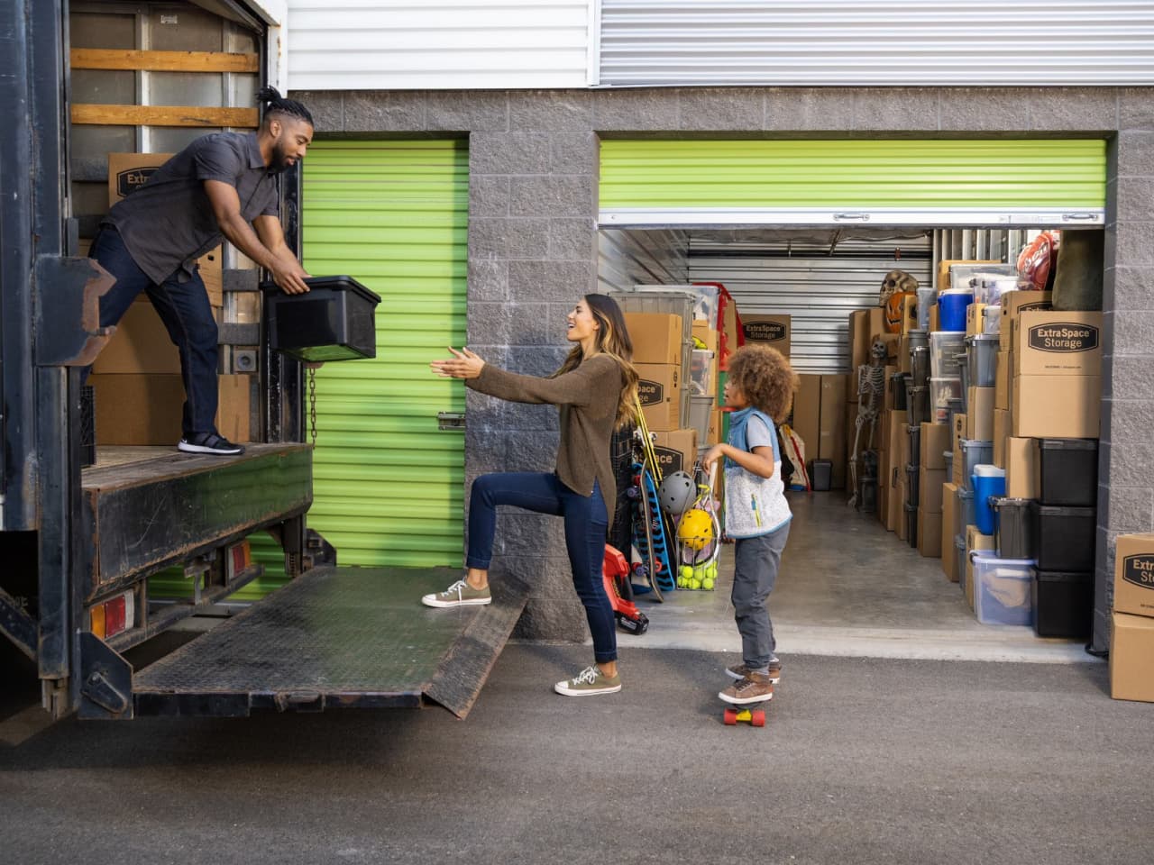 Family of three unloading boxes out of a moving truck into a storage unit
