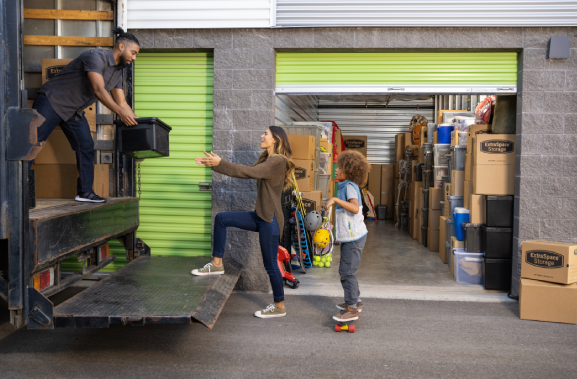 Family of three unloading boxes out of a moving truck into a storage unit 