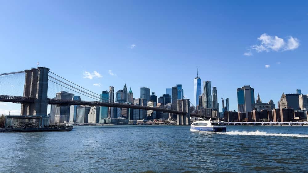 Boat going under bridge in New York City with skyscrapers in the background on a clear day