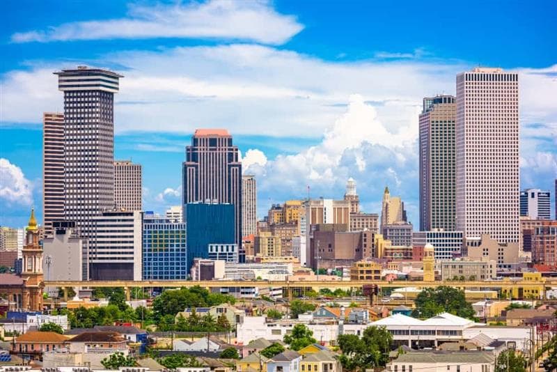 New Orleans skyline, featuring homes with trees between them in the foreground and a few skyscrapers in the background on a sunny day.