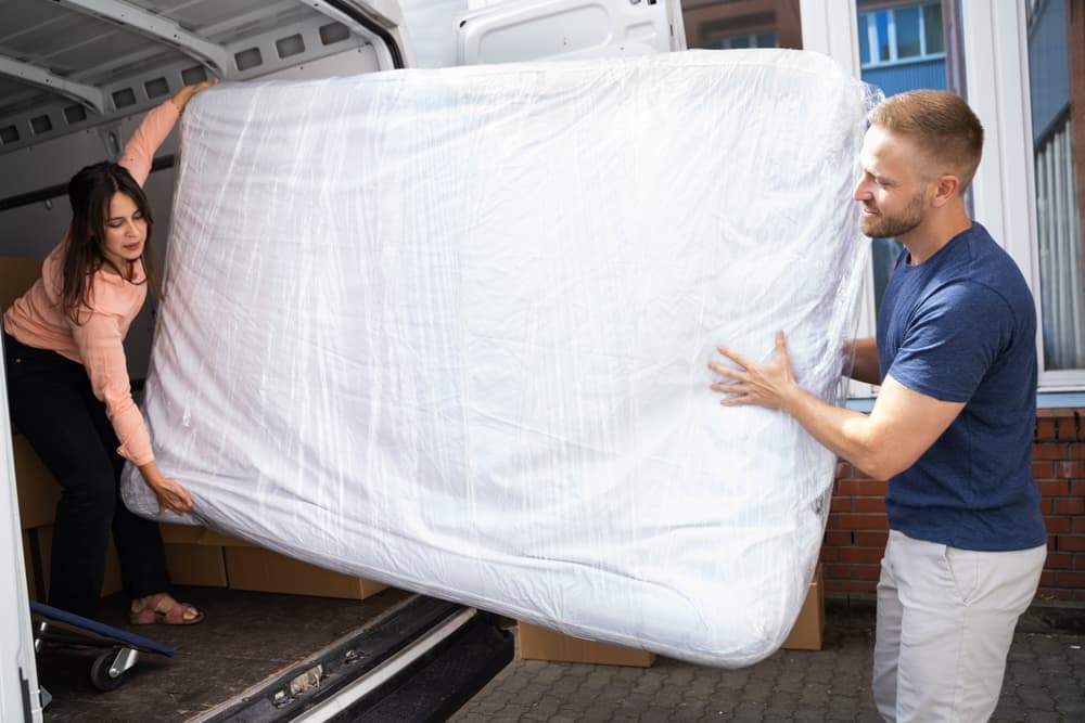 Woman and man moving covered mattress into moving van