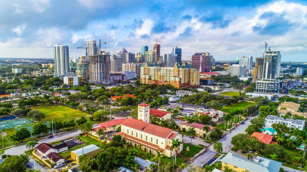 Aerial shot of Fort Lauderdale, Florida's downtown area during daytime, with blue skies and puffy white clouds.