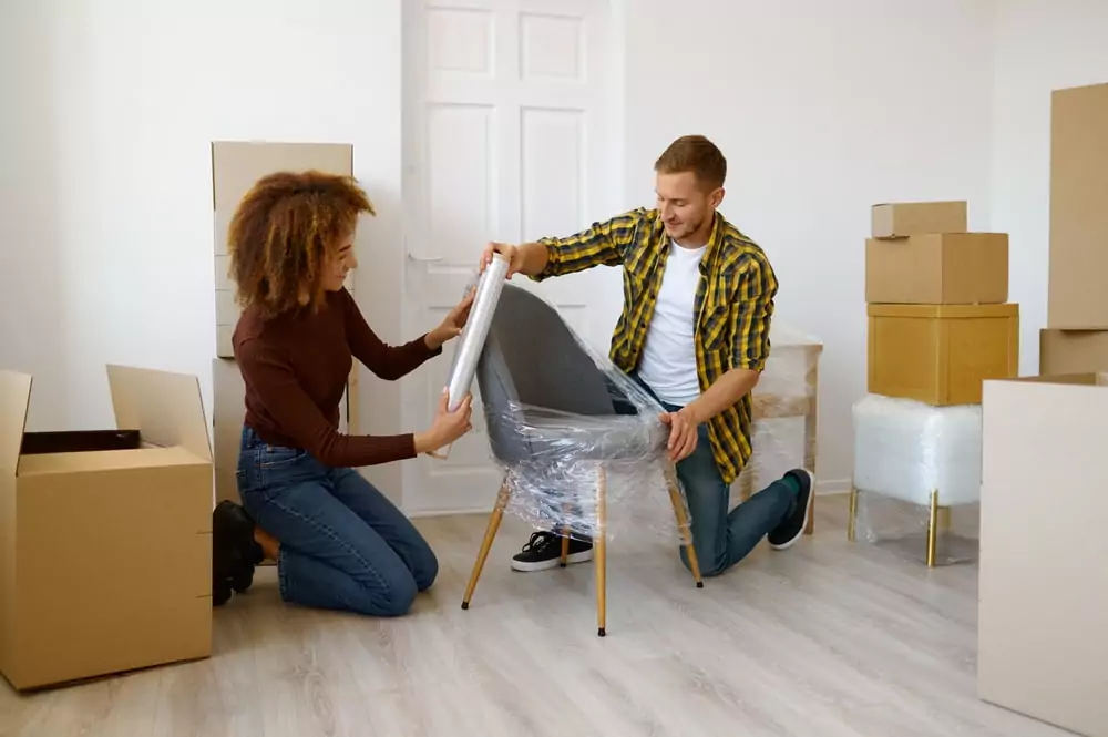 Two people wrapping a chair with packing wrap