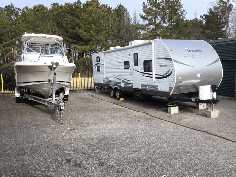 A boat and an RV in outdoor parking spots next to each other at a storage facility