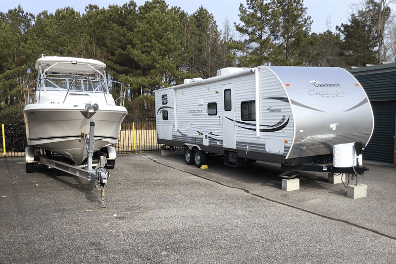 A boat and an RV in outdoor parking spots next to each other at a storage facility