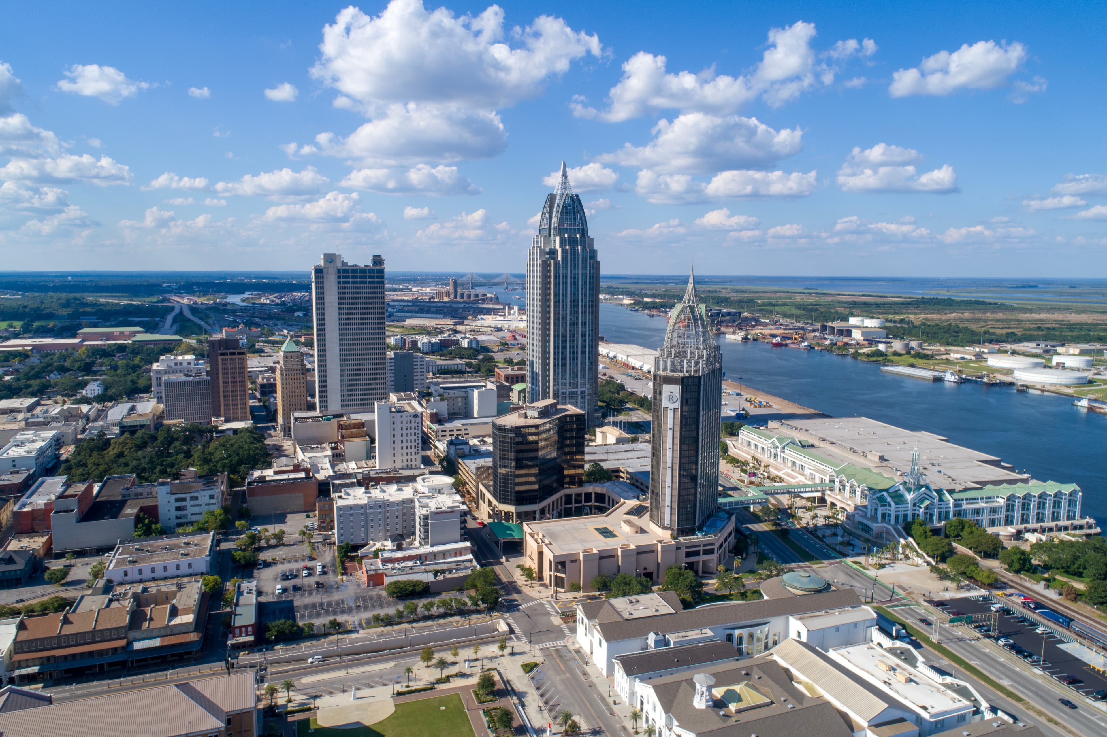 Aerial image of Mobile AL's downtown area on a sunny day, featuring blue skies and fluffy clouds.