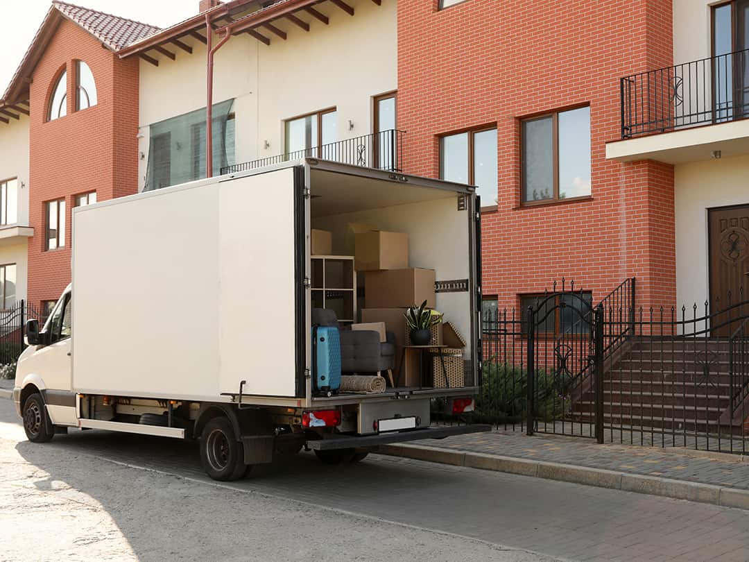 A moving truck parked outside of an apartment full of boxes and furnishings