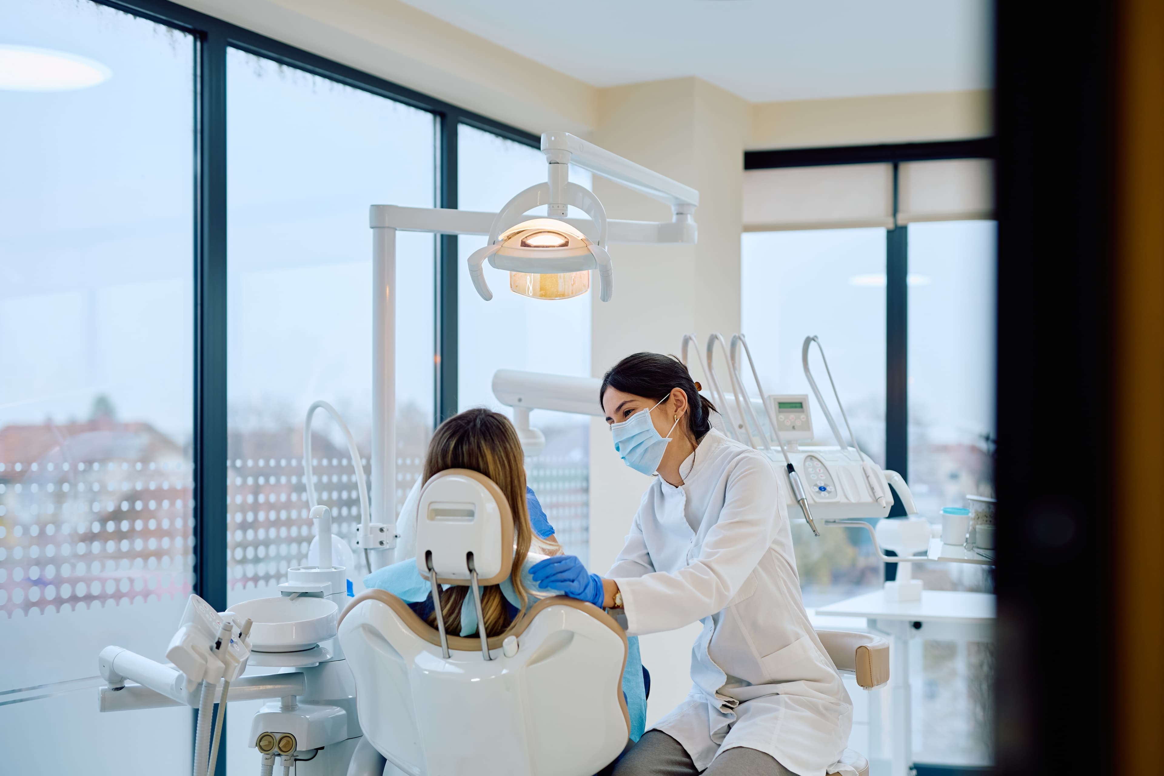 Dentist wearing a mask and gloves treating a patient reclined in a dental chair