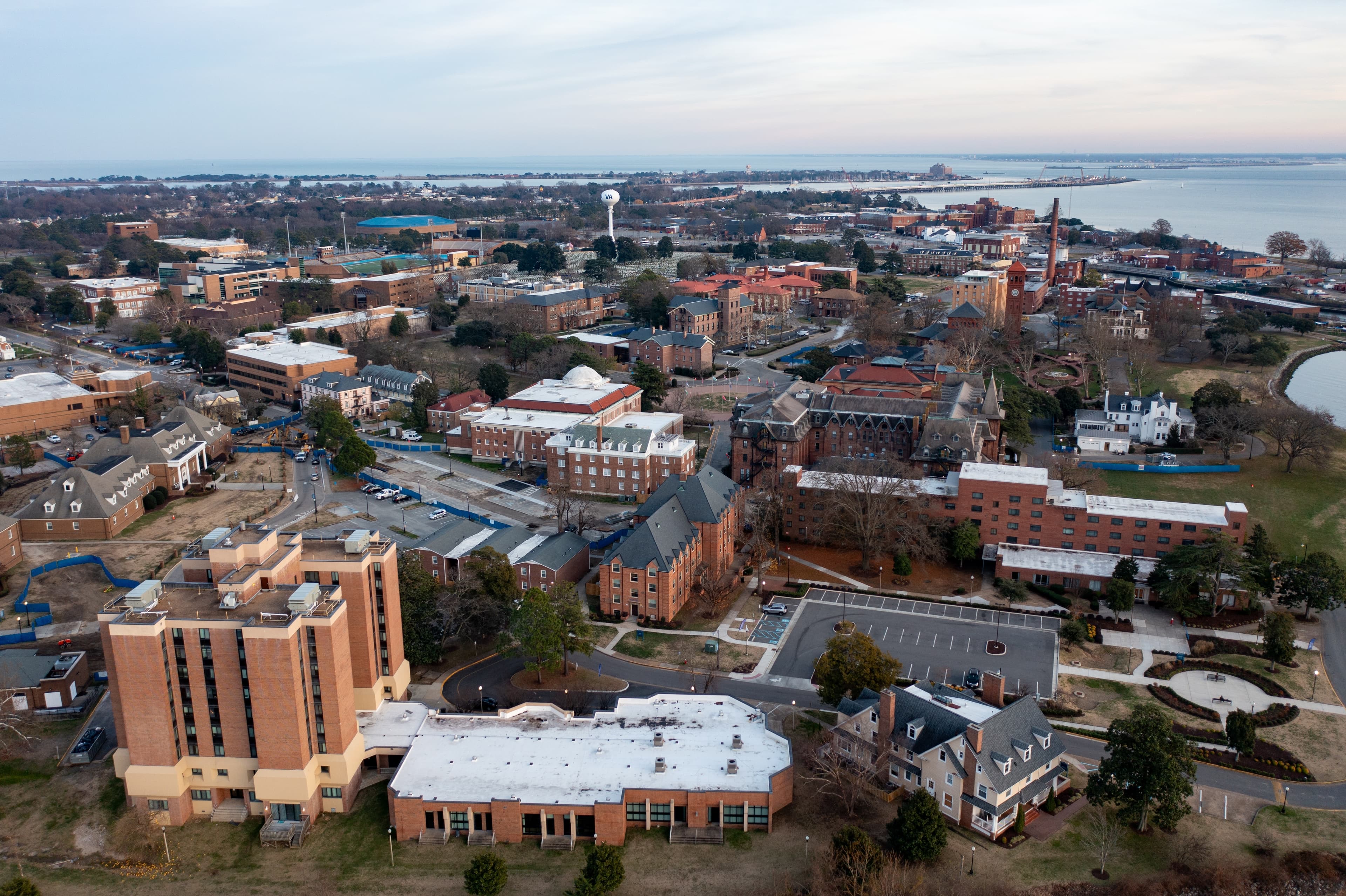 Overhead view of Hampton, VA featuring brick buildings at the city center, tree-lined busy streets, and Chesapeake Bay in the background.