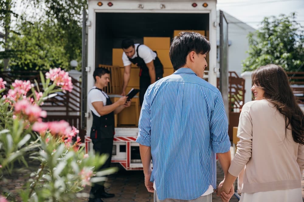 A man and a woman holding hands with movers in the background