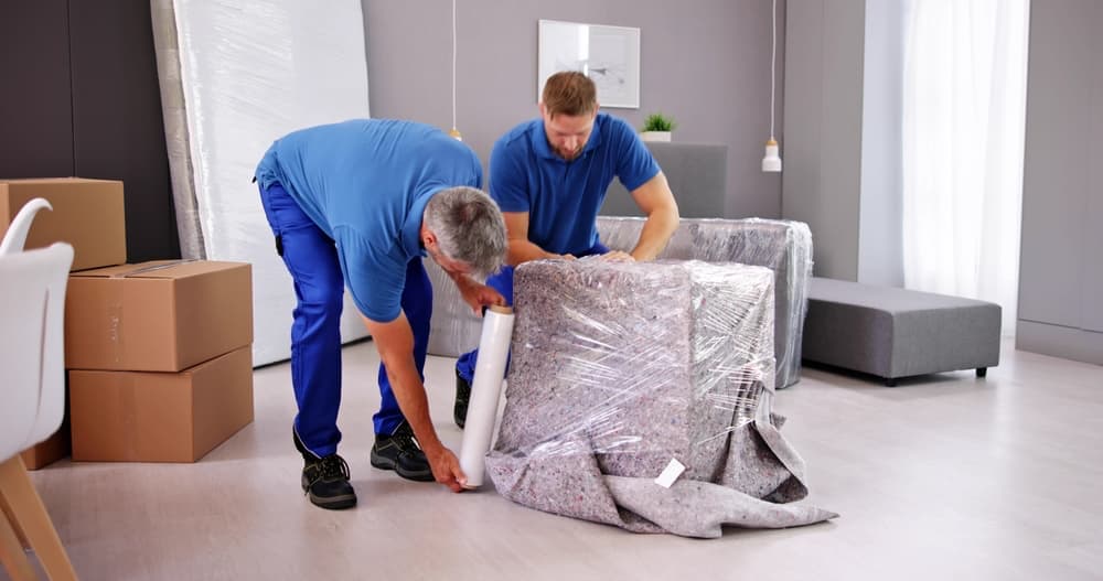 2 men wrapping a piece of furniture with protective moving supplies