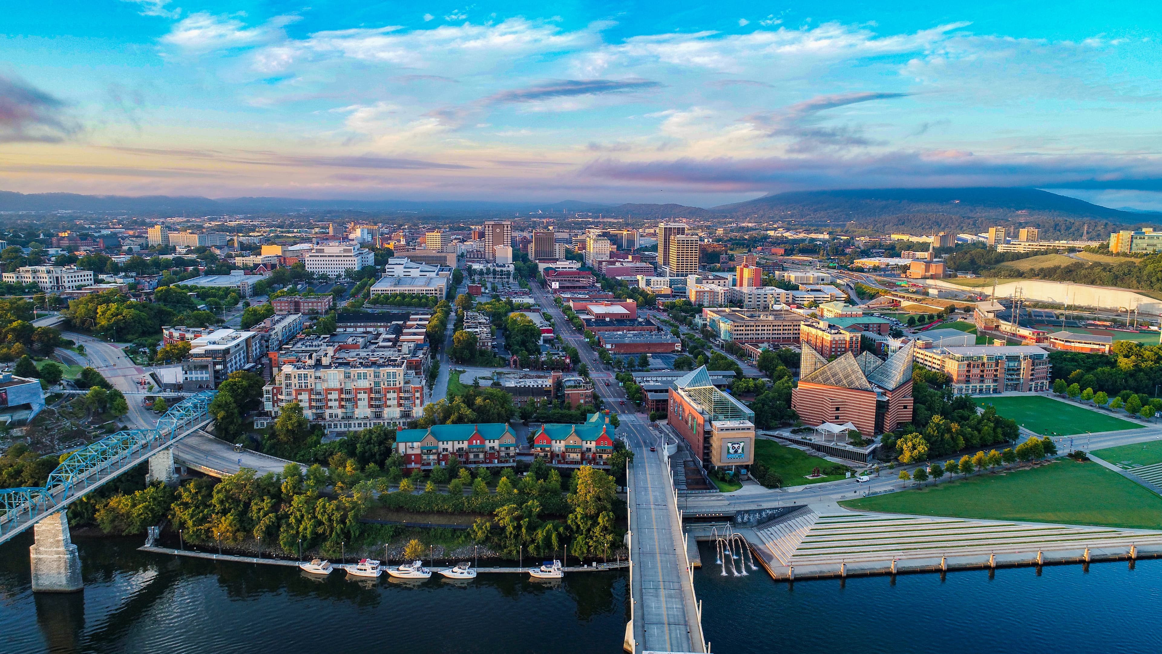 Overhead view of Chattanooga, TN at sunset with colorful buildings, tree-lined streets, and bridges across the Tennessee River.