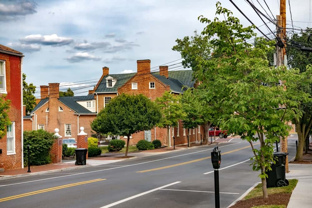 Main street in Winchester, VA featuring green trees, classic brick buildings, and a partly cloudy sky.
