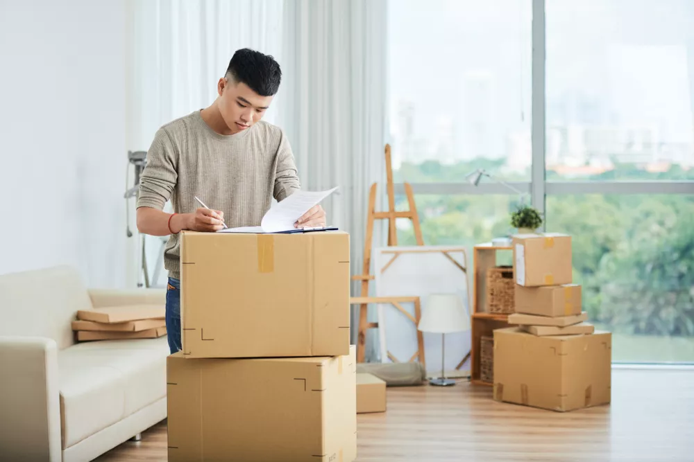Man filling out paperwork on top of packed boxes in a bright living room