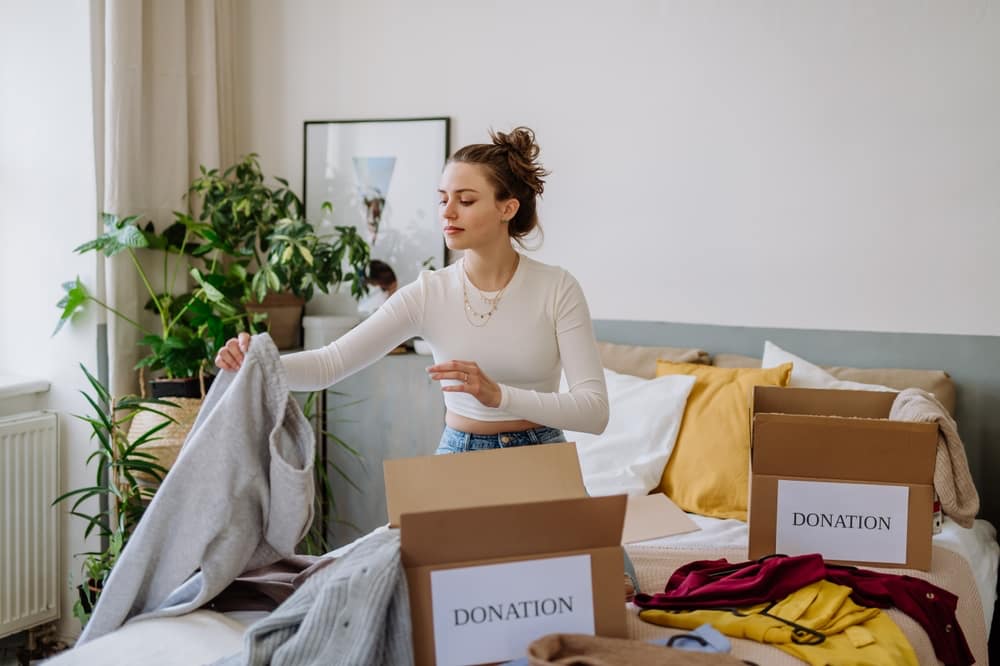 Woman packing clothes into donation boxes on bed in order to declutter before moving
