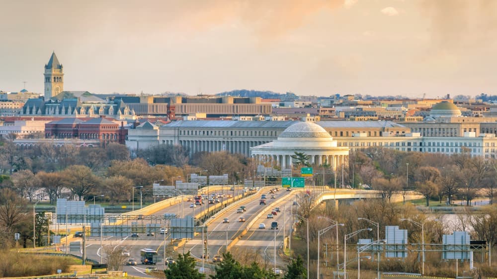 Skyline of Washington, DC in the morning on a partly cloudy day with a large interstate running through the middle and buildings in the background.