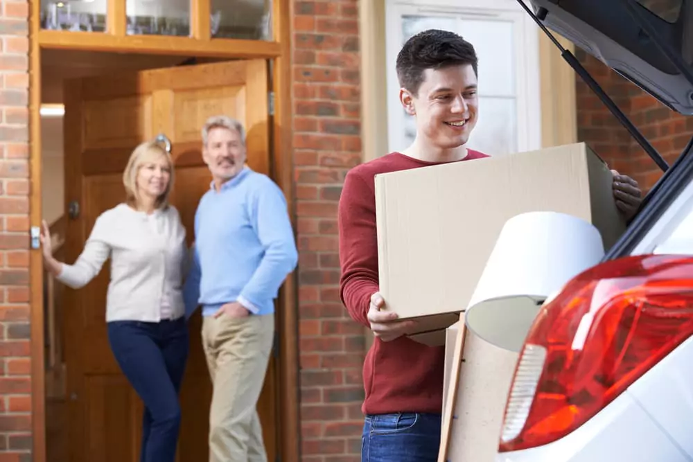 A young man putting a box into a trunk of a car