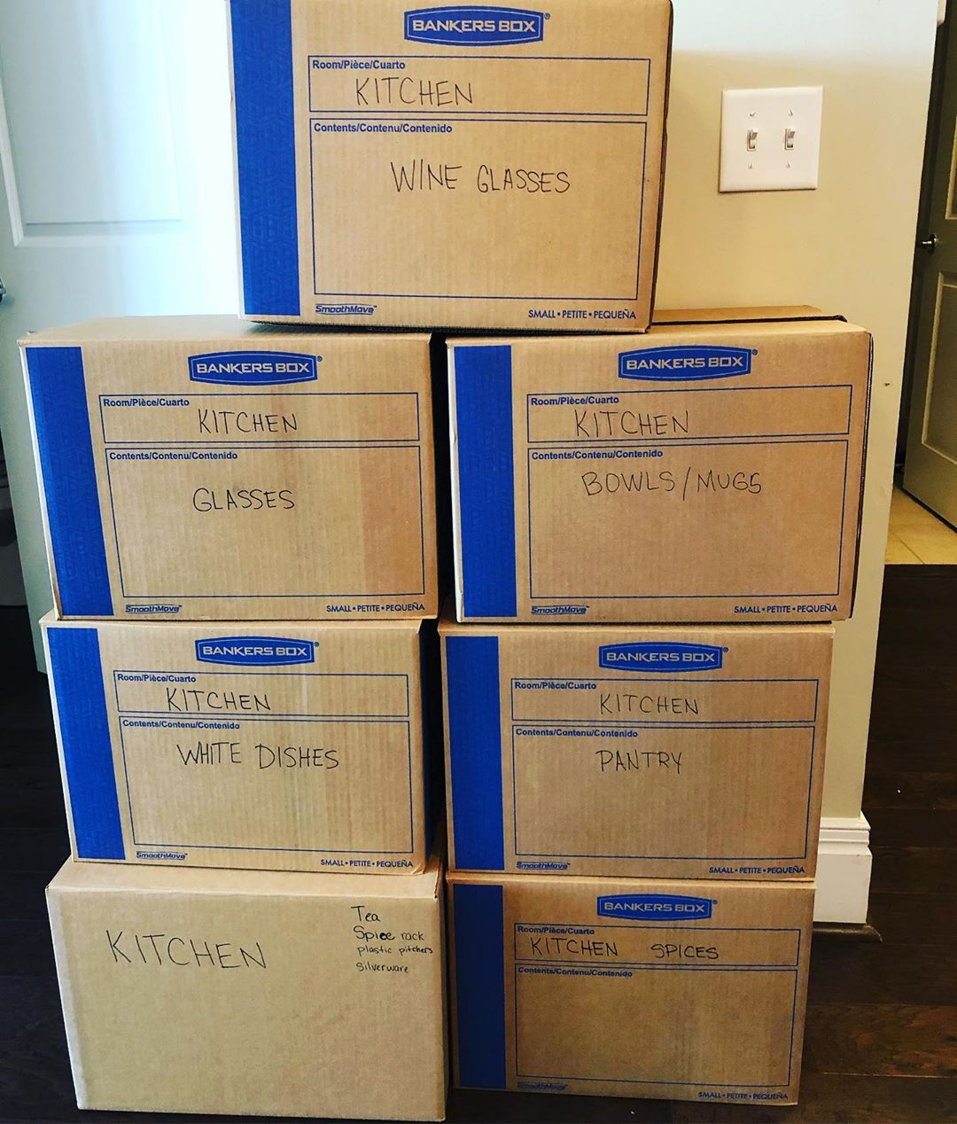 Moving boxes stacked against wall with labels by room. Photo by Instagram user @chaos.organizer