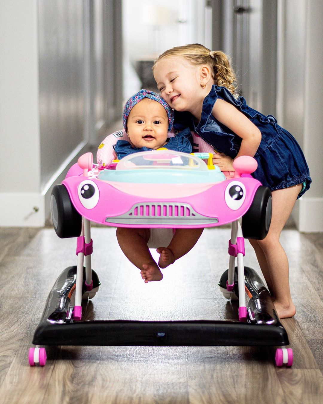 Baby in baby walker next to big sister. Photo by Instagram user @vivimccoy_