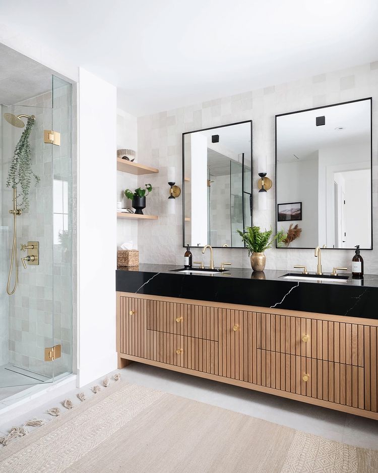 Dark countertops, light wood lower cabinets, and whit tiling in a bright bathroom. Photo by Instagram user @weltondesigngroup