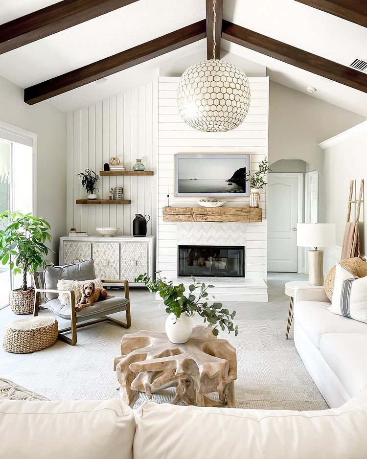 Open and naturally lit living room with dark wood beams and a neutral tan and white color palette. Photo by Instagram user @dabblingindecorating