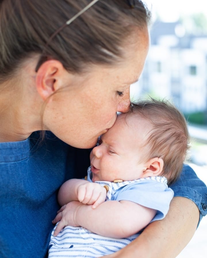 Mom kissing top of newborn's head. Photo by Instagram user @embecphoto