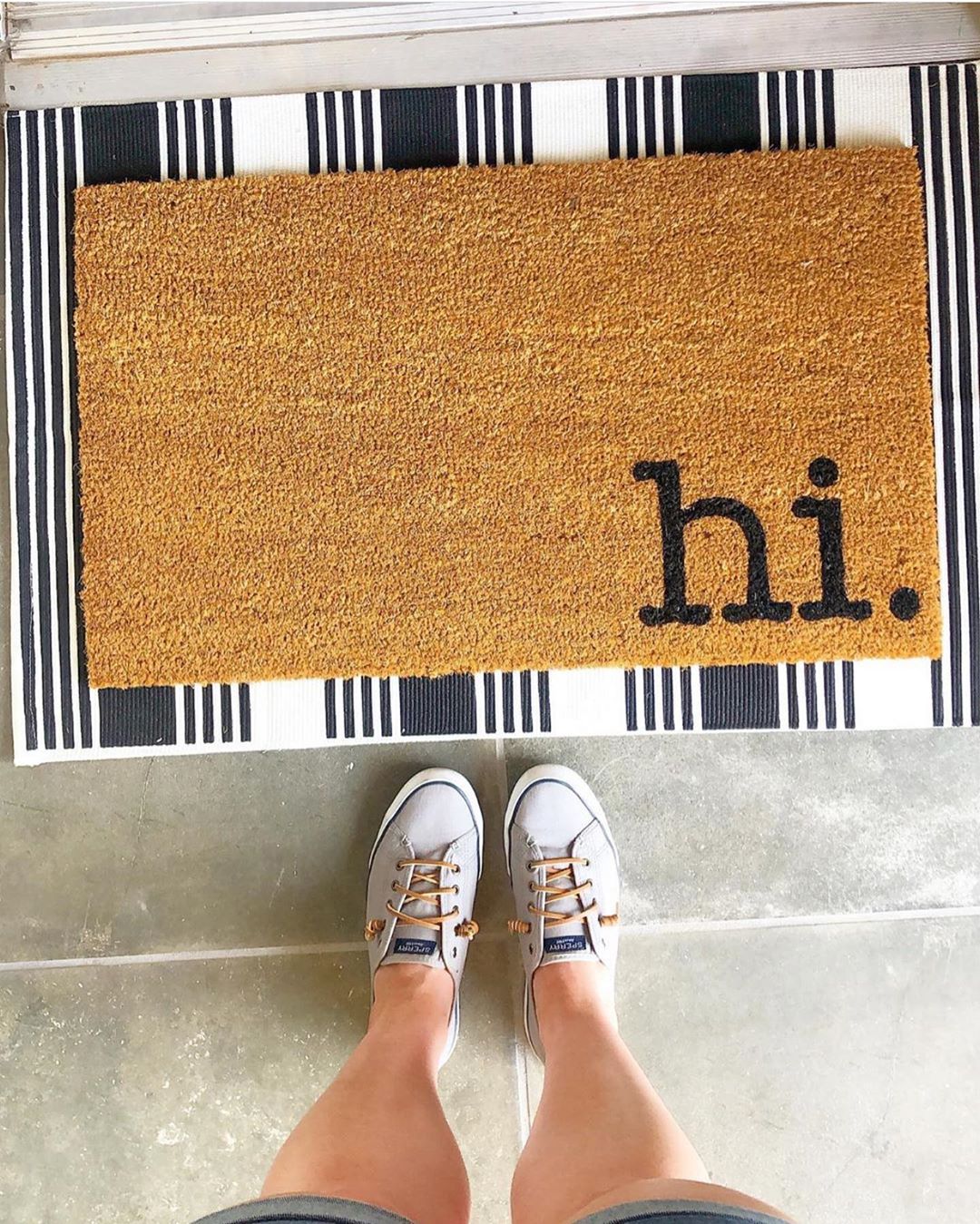 Woman standing before "hi" welcome door mat. Photo by Instagram user @blackandwheatco