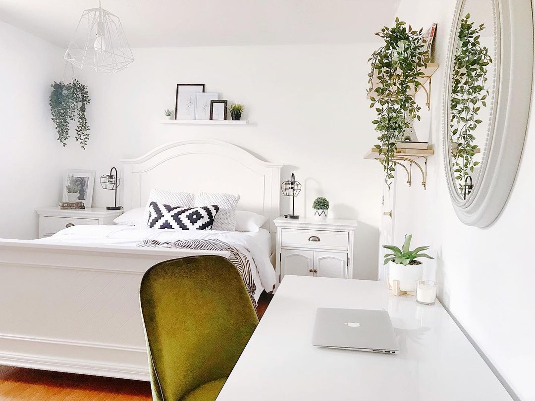 A modern bedroom in all white with green accents on the desk chair and plants. Photo via Instagram user @my_passion_for_decor