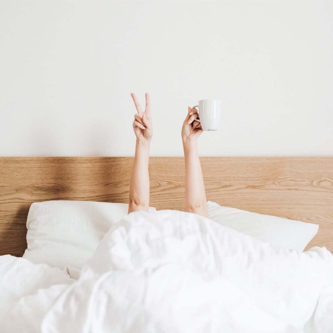 Woman lying in bed with coffee cup and peace sign fingers. Photo by Instagram user @rhondahamel.ca