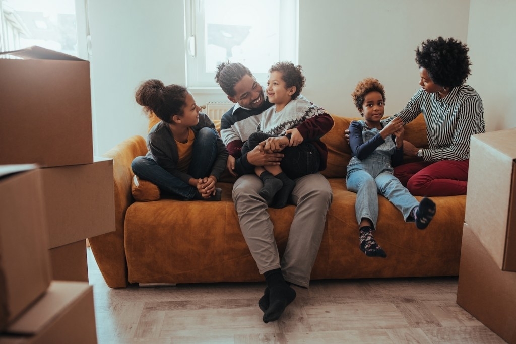 Family sitting on a couch surrounded by moving boxes. Photo by Instagram user @gruntsmovejunk_moving