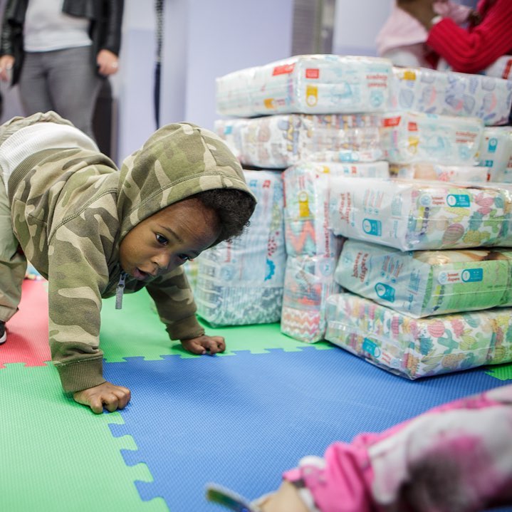 Young Child Crawling in Front of Stack of Donated Packs of Diapers. Photo by Instagram user @nycmammasgiveback