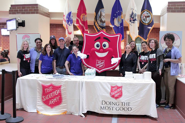 Volunteers and Mascot Behind a Table at a Booth for the Salvation Army. Photo by Instagram user @salvationarmyny