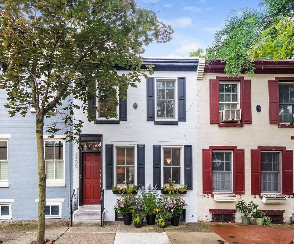 Two story white brick townhome with navy blue shutters and red door. Photo via Instagram user @ssellsphilly