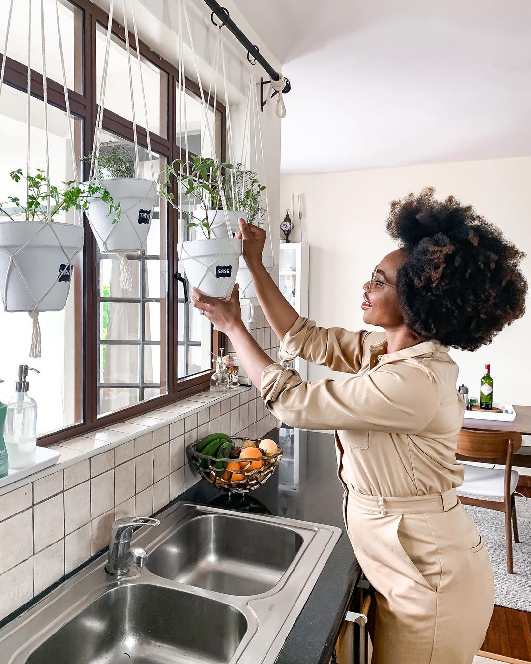 A woman hanging another pot in a hanging indoor herb garden. Photo by Instagram user @ijeomakola